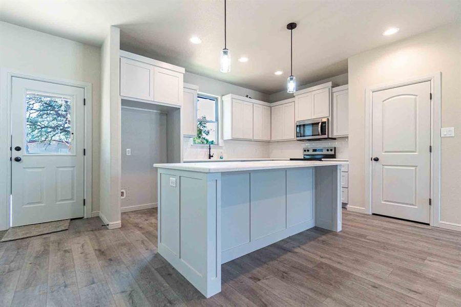 Kitchen with hanging light fixtures, white cabinetry, appliances with stainless steel finishes, light wood-type flooring, and a kitchen island