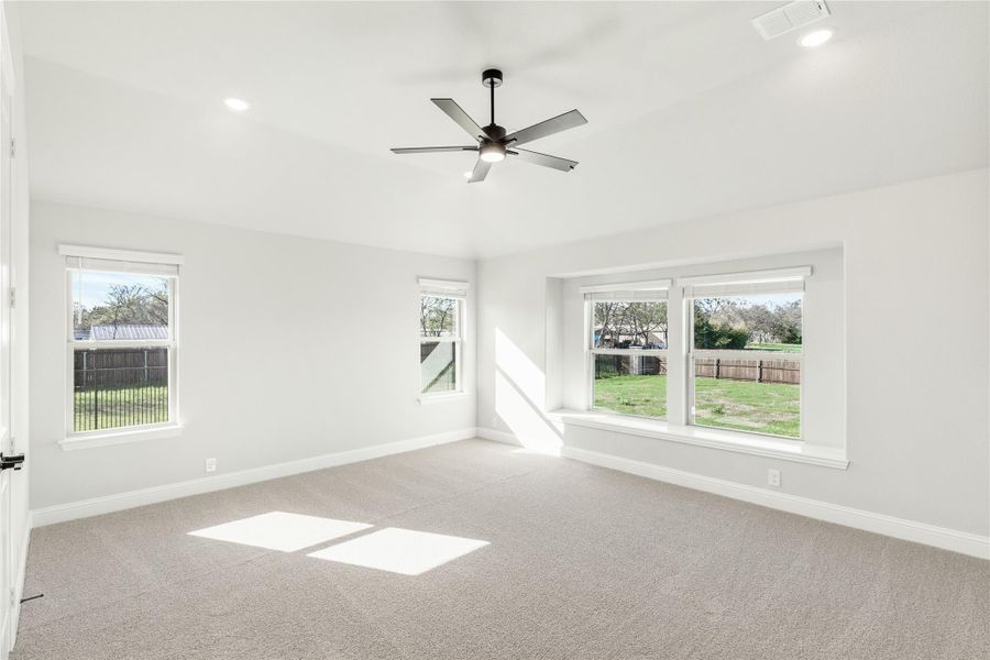 Empty bedroom with carpet, ceiling fan, and multiple windows overlooking a backyard Empty bedroom with carpet, ceiling fan, and multiple windows overlooking a backyard