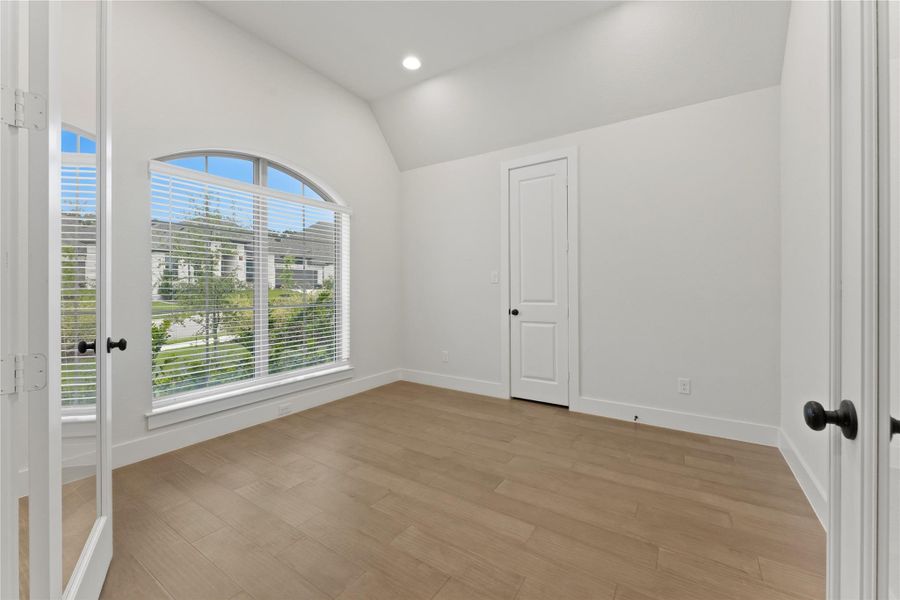 Room with arched window featuring horizontal blinds, wood-finish flooring, recessed lighting, and a white paneled door with black hardware