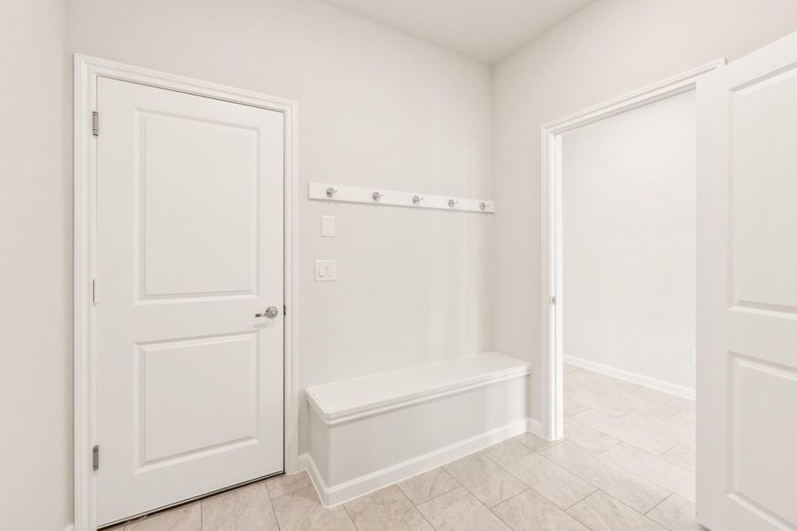 Mudroom with built-in bench, wall-mounted coat hooks, and light tile flooring Mudroom with built-in bench, wall-mounted coat hooks, and light tile flooring