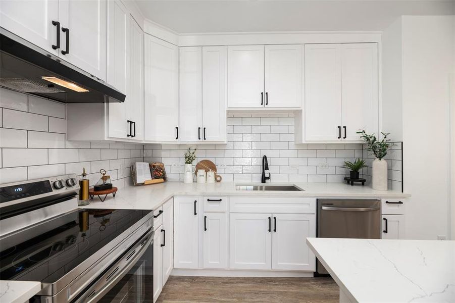 Kitchen featuring appliances with stainless steel finishes, white cabinetry, light stone countertops, range hood, and light wood-style floors Kitchen featuring appliances with stainless steel finishes, white cabinetry, light stone countertops, range hood, and light wood-style floors