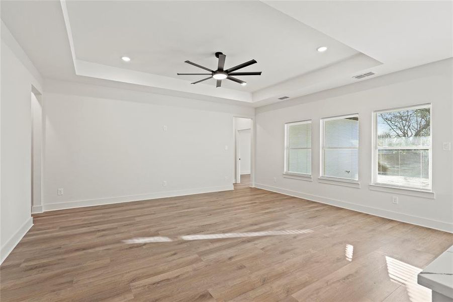 Unfurnished room featuring light wood finished floors, visible vents, a tray ceiling, and baseboards