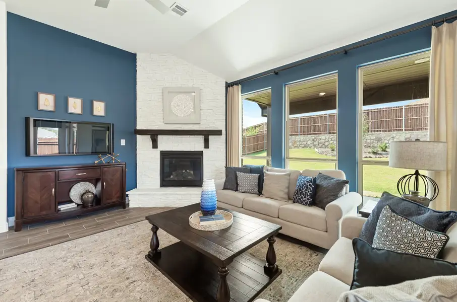 Living room with blue accent walls, white brick fireplace, beige sofas, and large windows overlooking a backyard