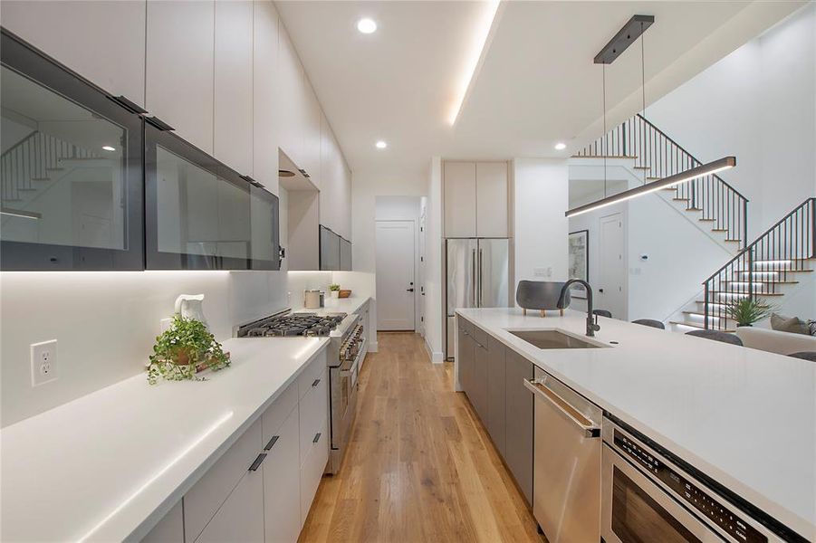 Kitchen featuring white cabinets, sink, decorative light fixtures, light hardwood / wood-style flooring, and premium appliances