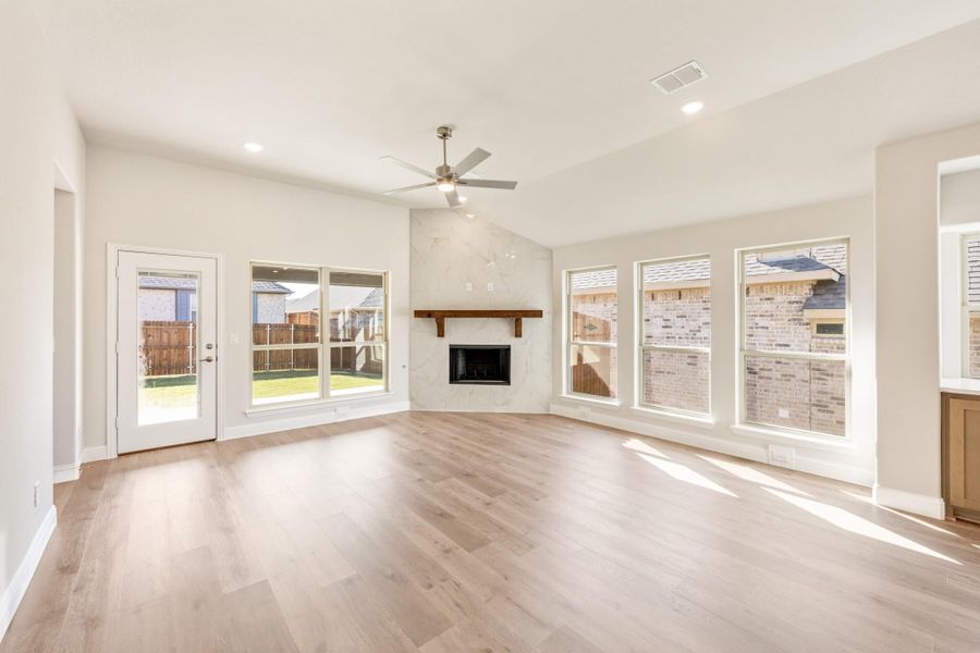 Open living room with light wood floors, marble fireplace, ceiling fan, and large windows Open living room with light wood floors, marble fireplace, ceiling fan, and large windows