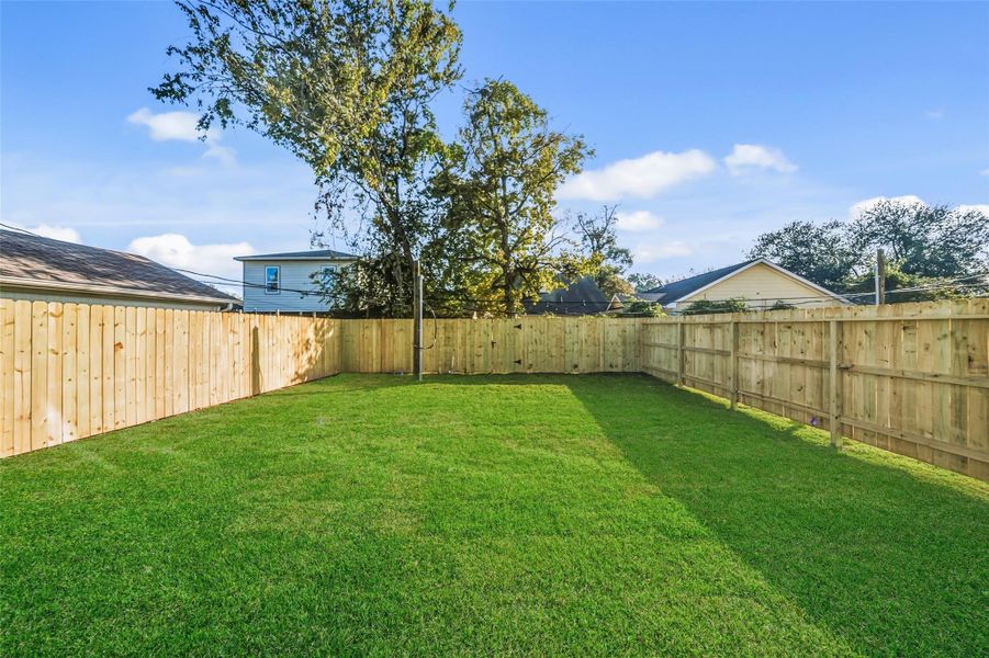 This photo shows a spacious backyard with well-maintained green grass, enclosed by a wooden privacy fence. A few trees are visible, providing a serene and private outdoor space suitable for relaxation or entertaining.