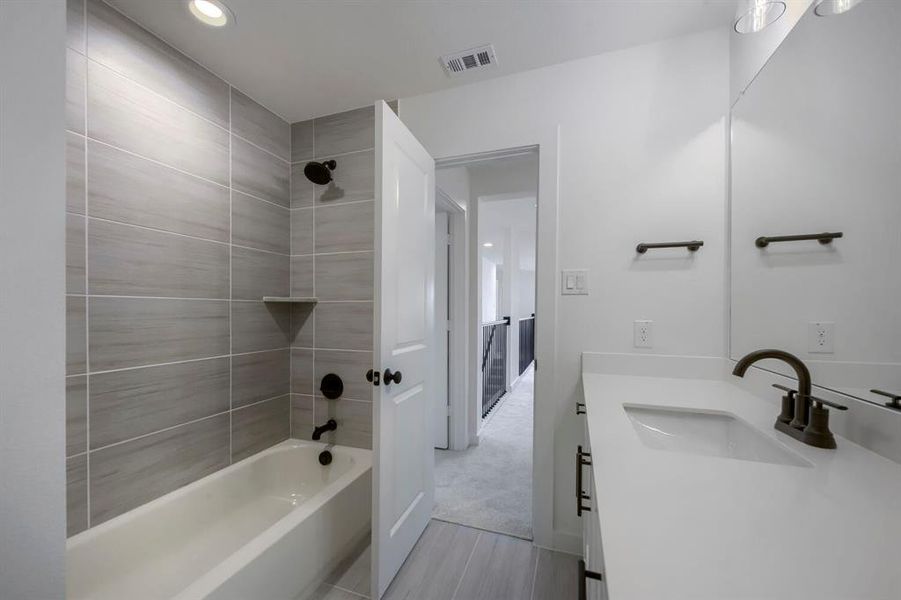 Bathroom featuring a tub/shower combination with grey horizontal tile surround, a built-in corner shelf, and matte black fixtures Bathroom featuring a tub/shower combination with grey horizontal tile surround, a built-in corner shelf, and matte black fixtures