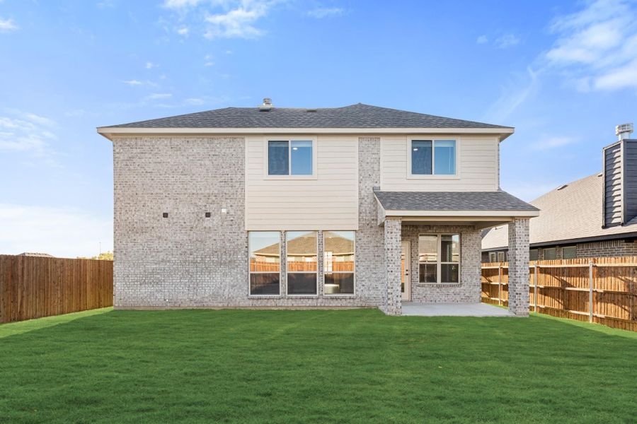 Two-story brick home rear exterior with covered patio, large windows, and fenced backyard with green lawn Two-story brick home rear exterior with covered patio, large windows, and fenced backyard with green lawn