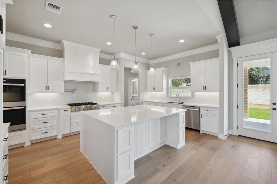 Kitchen featuring stainless steel appliances, custom range hood, light wood-type flooring, and a center island