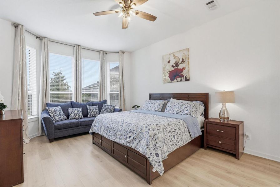 Relax in the spacious primary bedroom, featuring beautiful wood flooring, multiple windows with privacy blinds, and a ceiling fan, creating a bright, comfortable, and elegant space designed for rest and relaxation.