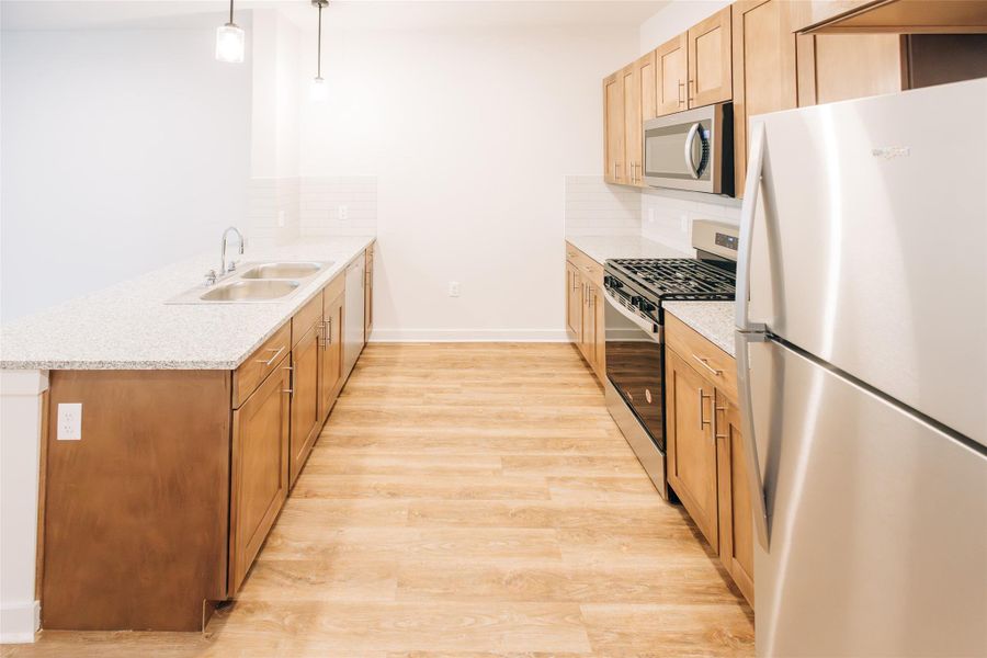 Kitchen featuring appliances with stainless steel finishes, a sink, a peninsula, light wood-type flooring, and decorative backsplash