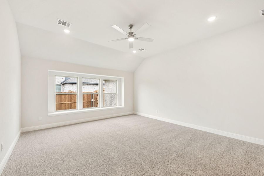 Empty bedroom with vaulted ceiling, ceiling fan, carpet flooring, and large window with backyard view