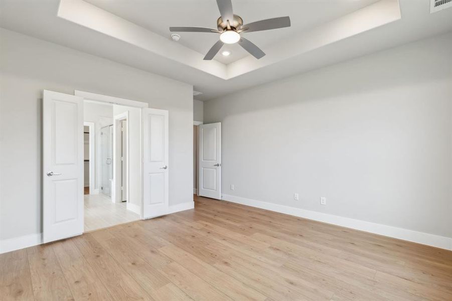 Unfurnished bedroom with a raised ceiling, ceiling fan, and light wood-type flooring