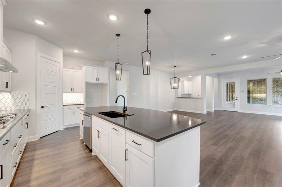 Kitchen with dark wood-style floors, white cabinets, a center island with sink, and open floor plan