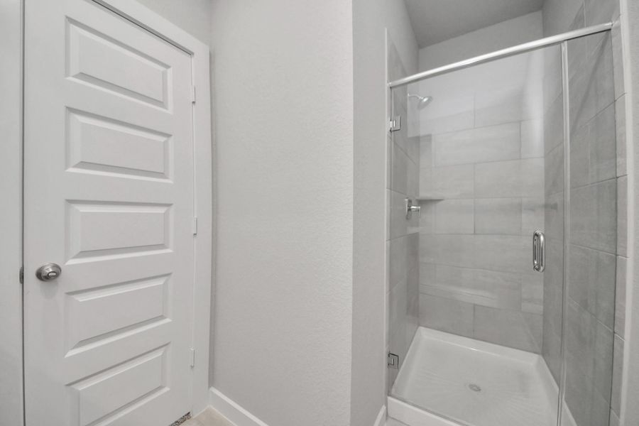 Secondary bath features tile flooring, a walk-in shower with tile surround, light stained wood cabinets, beautiful light countertop. Sample photo of completed home with similar floor plan. Actual colors and selections may vary.