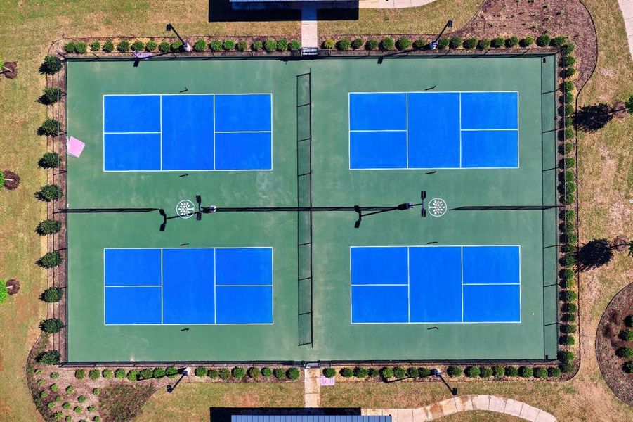 Four blue and green outdoor courts, surrounded by manicured landscaping and grass, offer recreational opportunities