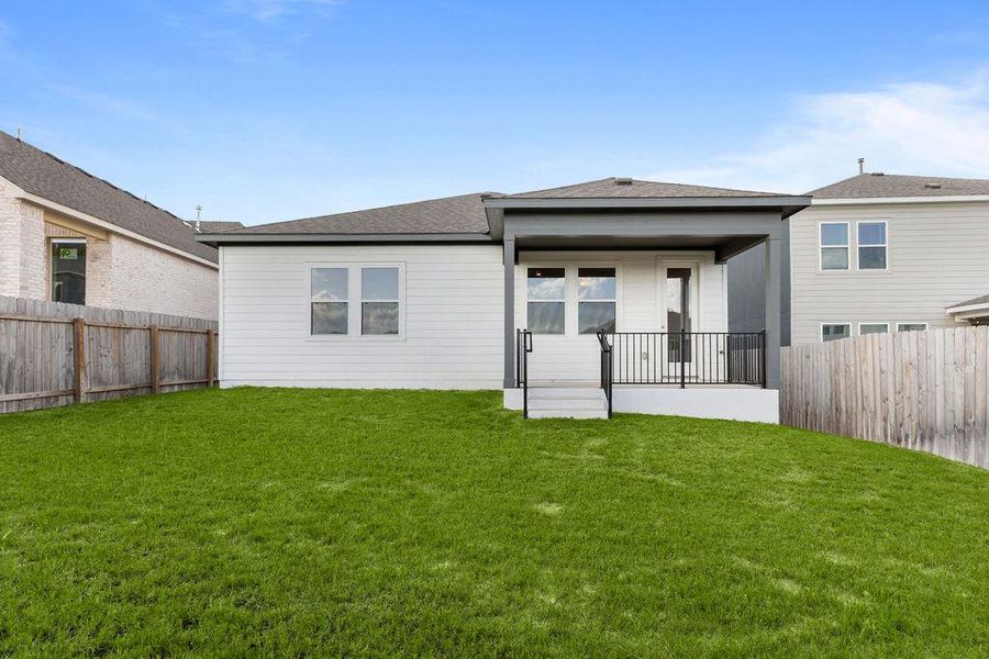 A well-maintained lawn stretches behind a newly constructed home featuring a covered patio. A well-maintained lawn stretches behind a newly constructed home featuring a covered patio.