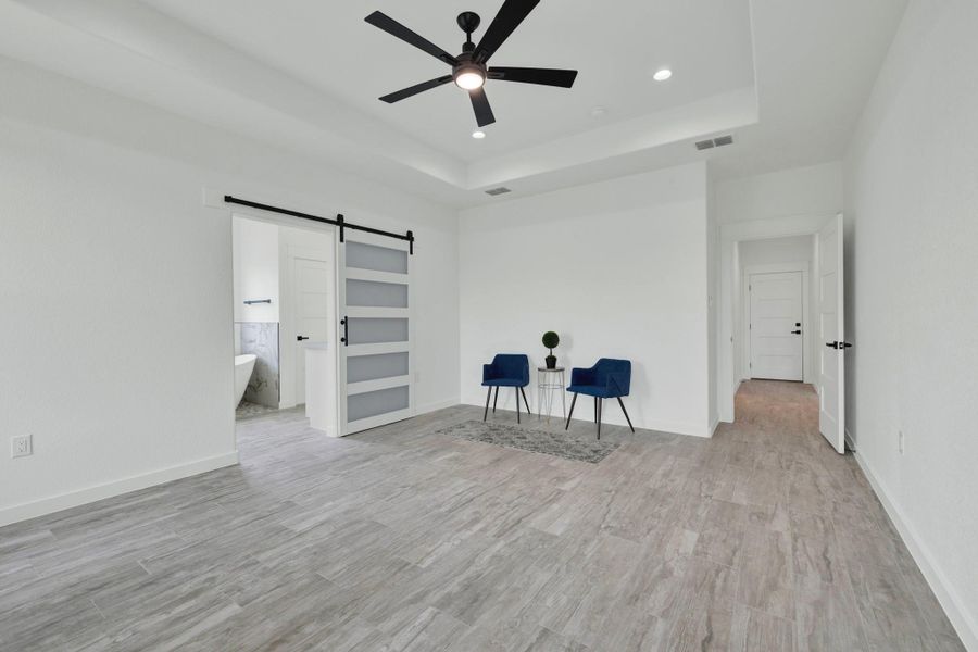 Spacious master bedroom featuring wood-finish tile flooring, a tray ceiling with a ceiling fan, and recessed lighting