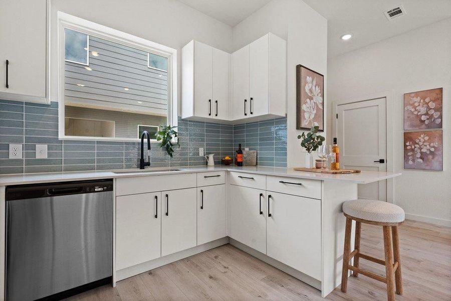Modern kitchen featuring white cabinetry with dark hardware, a stainless steel dishwasher, a white sink with a black faucet, and a blue tiled backsplash