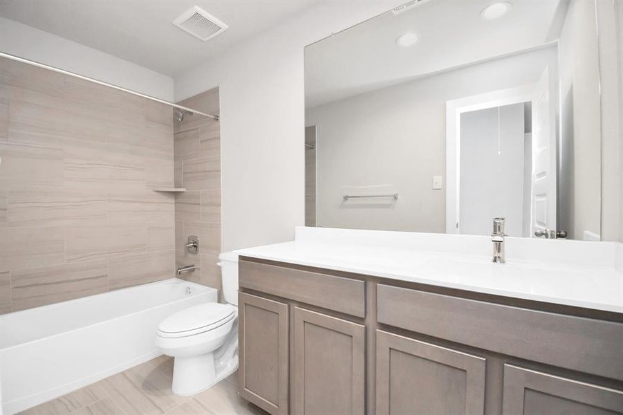 The secondary bath boasts stylish tile flooring, a bath/shower combo with a sleek tile surround, light wood cabinets, and a stunning light countertop. Sample photo of completed home with similar floor plan. Actual colors and selections may vary.