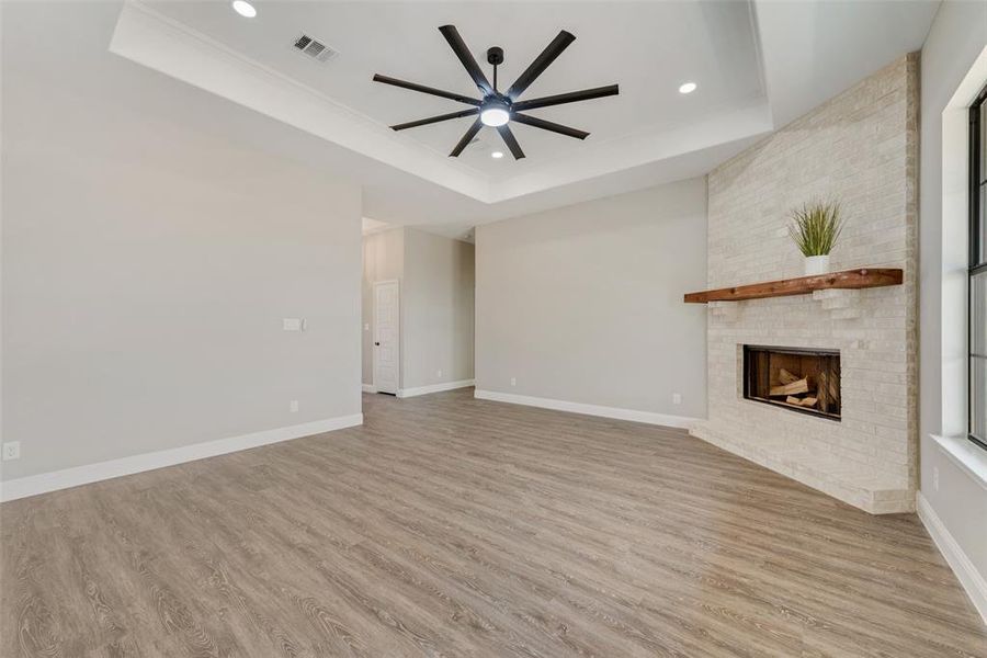 Unfurnished living room featuring ceiling fan, light hardwood / wood-style floors, a raised ceiling, and a brick fireplace