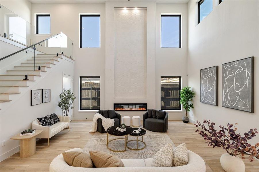 Living room featuring a towering ceiling, a healthy amount of sunlight, light hardwood / wood-style floors, and a fireplace