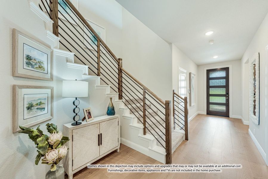 Bright entryway with staircase, wood railing, light hardwood floors, and dark front door with glass panels Bright entryway with staircase, wood railing, light hardwood floors, and dark front door with glass panels