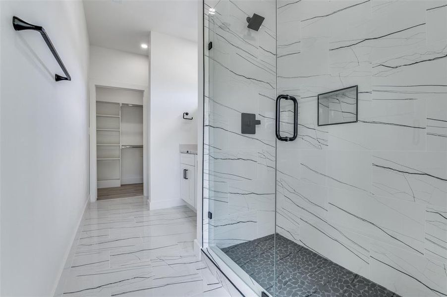 Full bathroom with marble look tile flooring, a marble finish shower, a spacious closet, and recessed lighting Full bathroom with marble look tile flooring, a marble finish shower, a spacious closet, and recessed lighting
