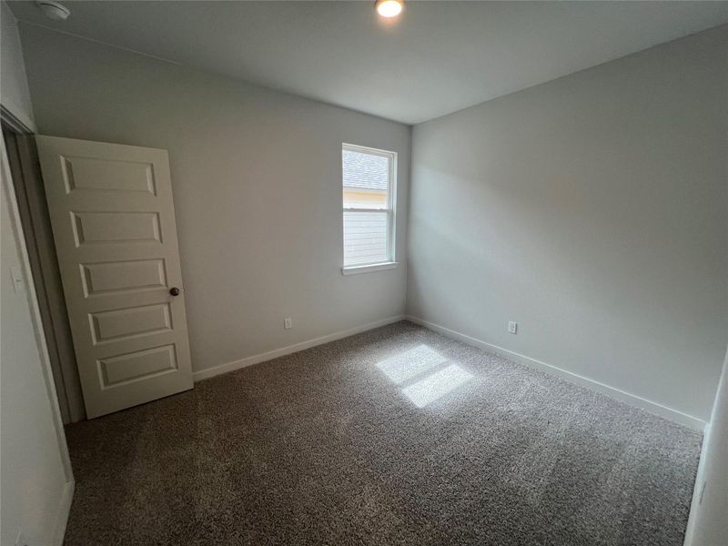 A well-lit bedroom features plush carpeting and a convenient single window.
