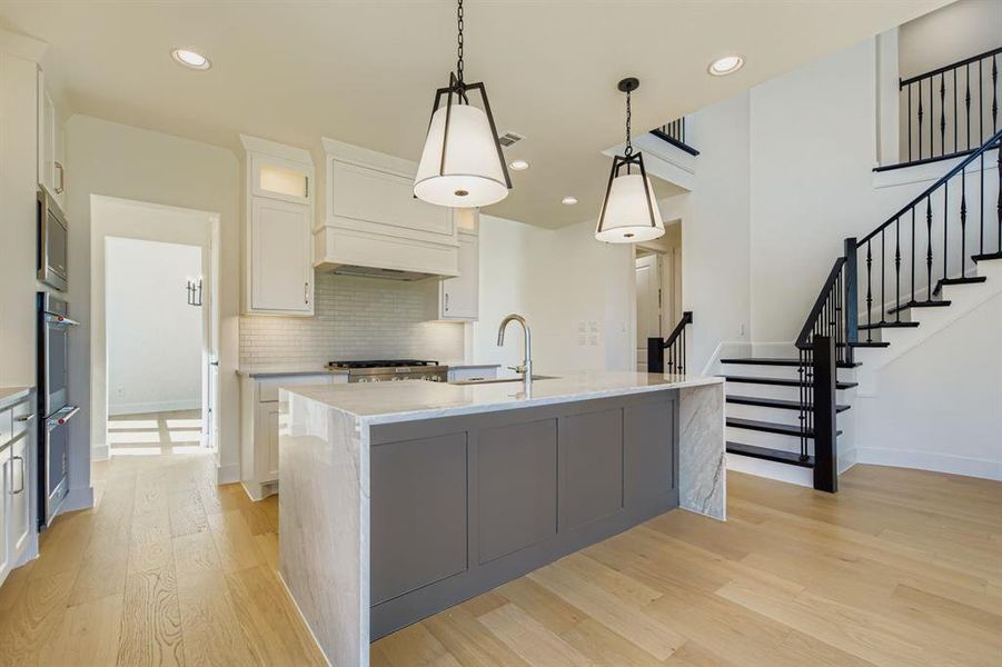 Kitchen featuring decorative backsplash, light stone countertops, hanging light fixtures, light wood finished floors, and white cabinetry Kitchen featuring decorative backsplash, light stone countertops, hanging light fixtures, light wood finished floors, and white cabinetry