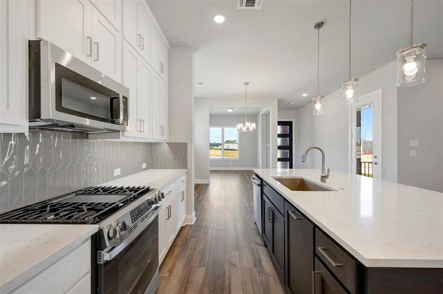 Kitchen with stainless steel appliances, dual tone cabinetry, dark wood finished floors, light stone counters, and an island with sink