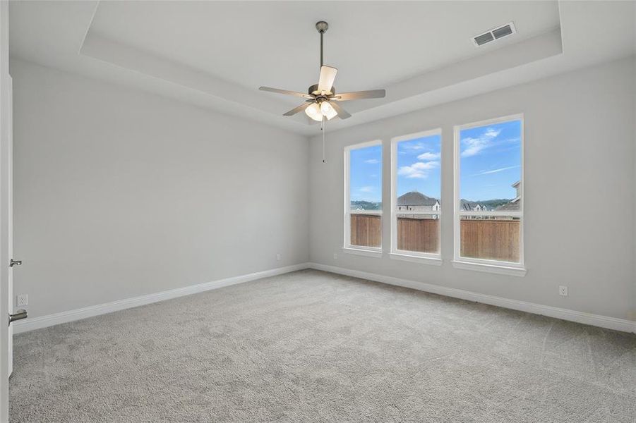 Carpeted empty room featuring baseboards, ceiling fan, and a tray ceiling
