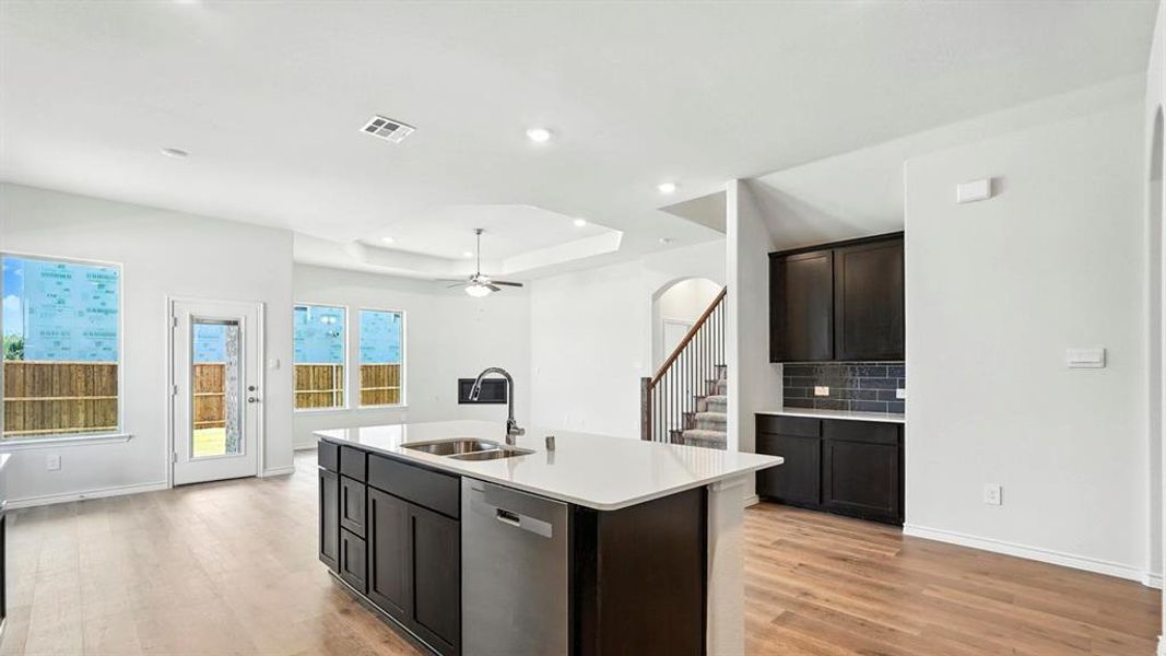 Kitchen with dishwasher, arched walkways, a center island with sink, light wood-style flooring, and light stone countertops