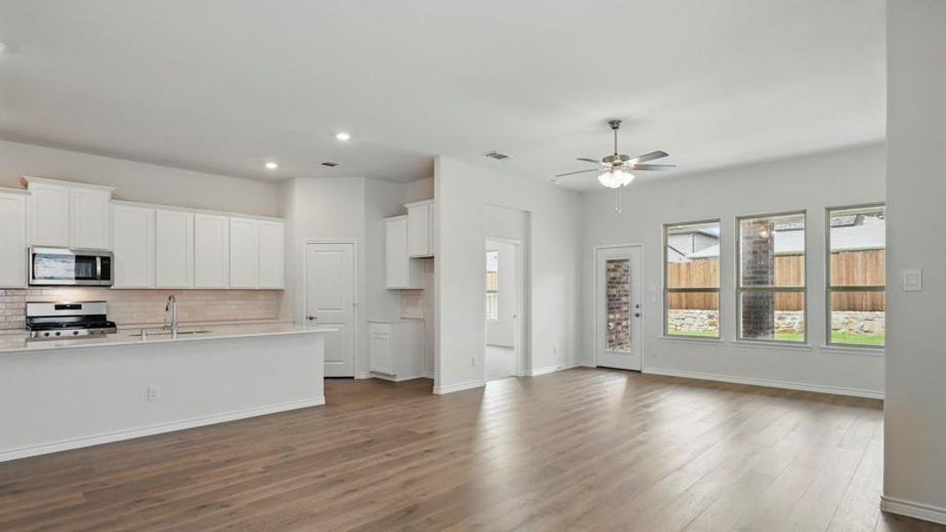 Open concept living area featuring wood-finish flooring throughout, a modern kitchen with white cabinetry and light-toned countertops, stainless steel appliances, and a tile backsplash
