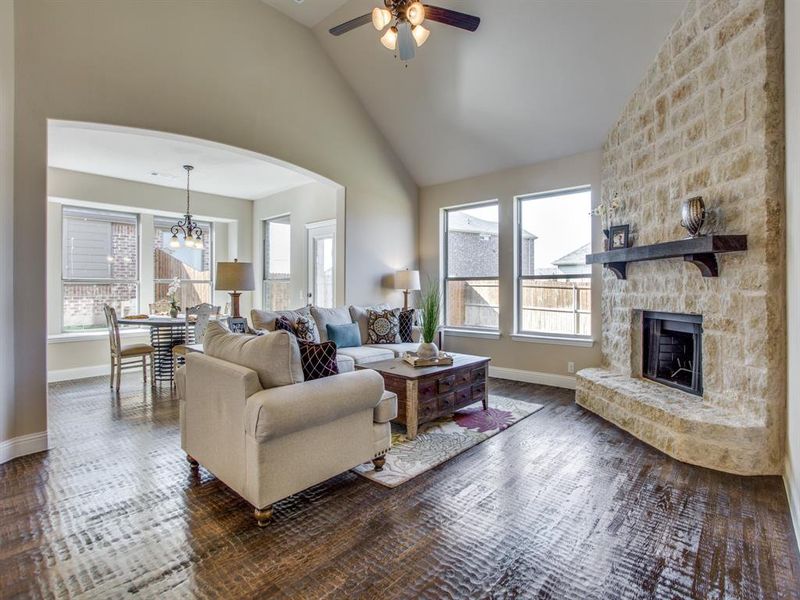 Living room with ceiling fan with notable chandelier, a fireplace, high vaulted ceiling, and a wealth of natural light