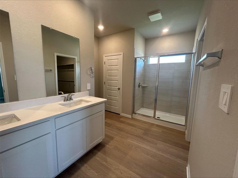 Bathroom with a stall shower, wood finished floors, double vanity, a spacious closet, and recessed lighting Bathroom with a stall shower, wood finished floors, double vanity, a spacious closet, and recessed lighting