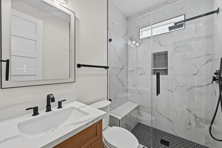 Elegant bathroom featuring a sleek glass-enclosed shower with marble-style tiles, a modern vanity with black fixtures, and a spacious mirror for a luxurious feel.
