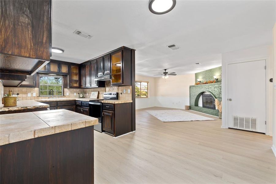 Kitchen with glass insert cabinets, dark brown cabinets, tasteful backsplash, and electric range