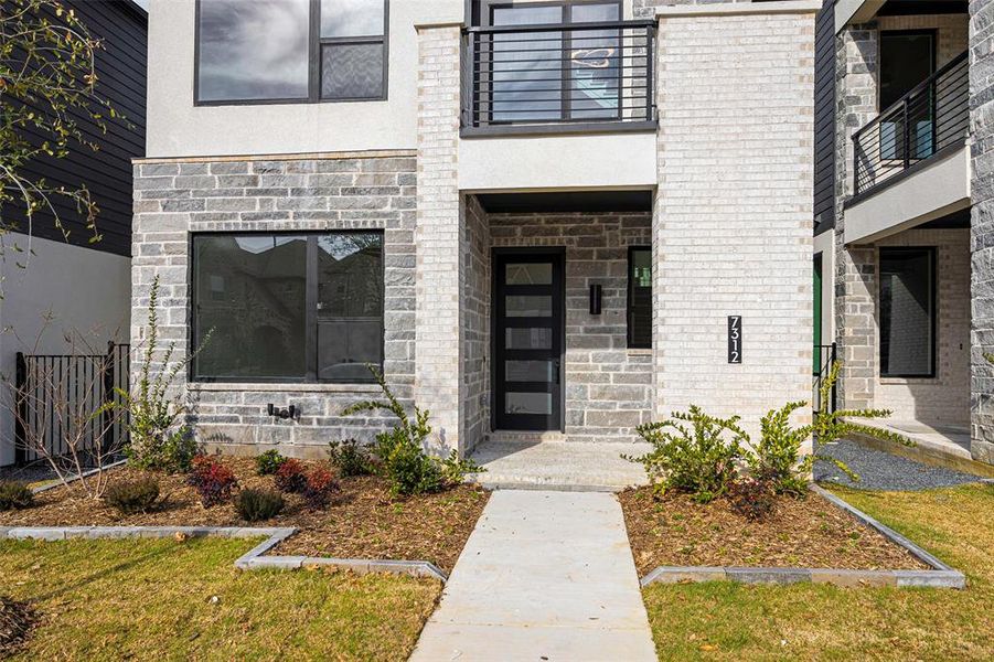 View of exterior entry featuring a balcony, stucco siding, and brick siding