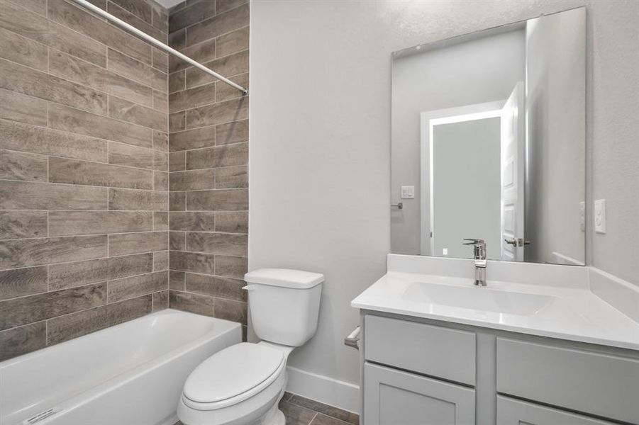 Secondary bath features tile flooring, bath/shower combo with tile surround, light stained wood cabinets, beautiful light countertop, and modern harware. Sample photo of completed home with similar plan. As built color and selections will vary.