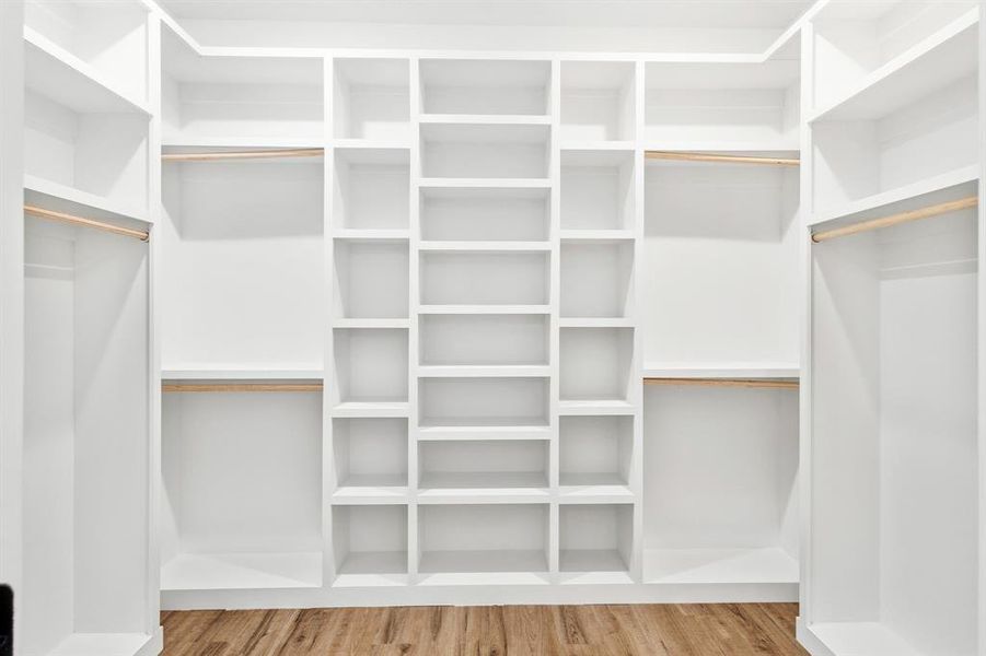 Built-in white shelving system with multiple compartments and hanging rods, set against wood-finish flooring Built-in white shelving system with multiple compartments and hanging rods, set against wood-finish flooring
