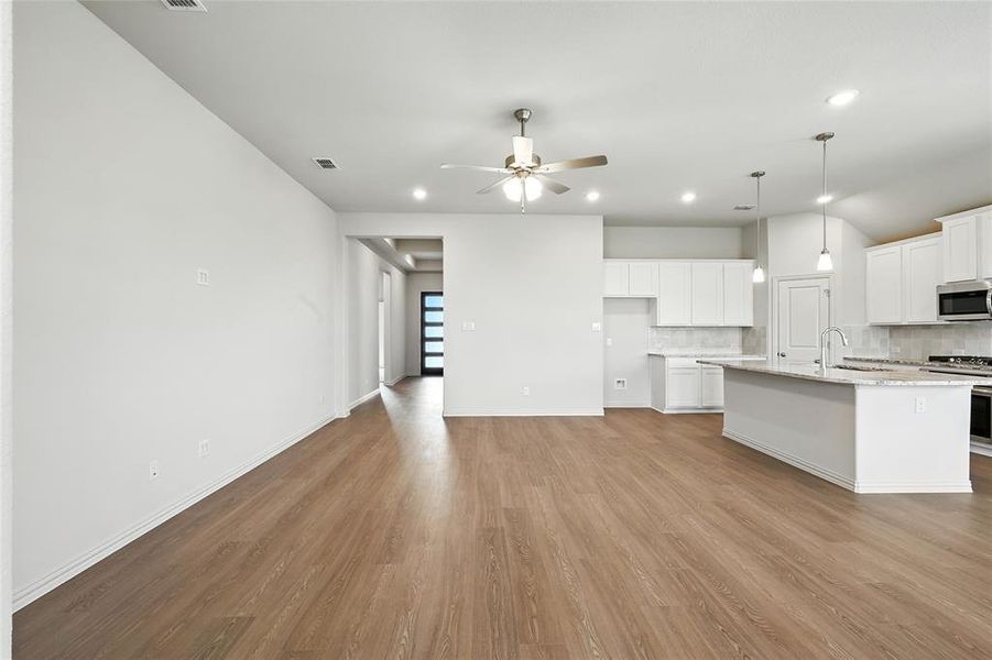 Kitchen with white cabinetry, decorative backsplash, light wood-style flooring, an island with sink, and decorative light fixtures Kitchen with white cabinetry, decorative backsplash, light wood-style flooring, an island with sink, and decorative light fixtures