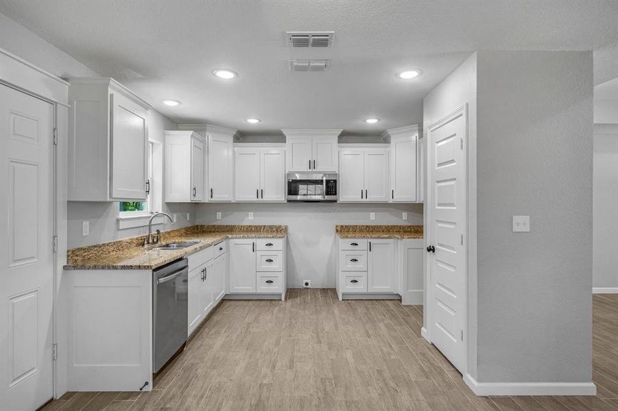 Kitchen featuring white cabinets, light wood-style flooring, dark stone countertops, appliances with stainless steel finishes, and recessed lighting Kitchen featuring white cabinets, light wood-style flooring, dark stone countertops, appliances with stainless steel finishes, and recessed lighting