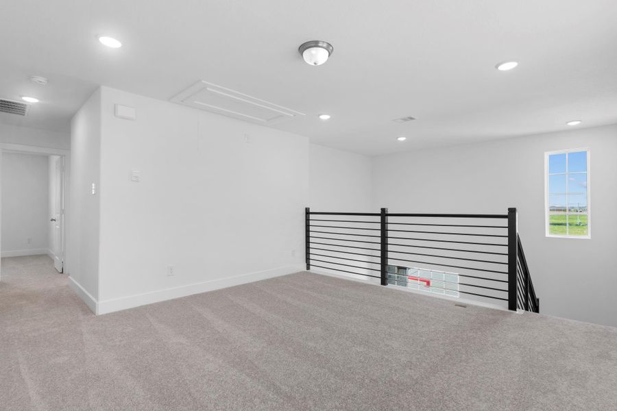 Additional angle of the upstairs game room showcasing the sleek railing design and abundant natural light.  Down the hallway you will discover tucked away the three guest bedrooms and more!