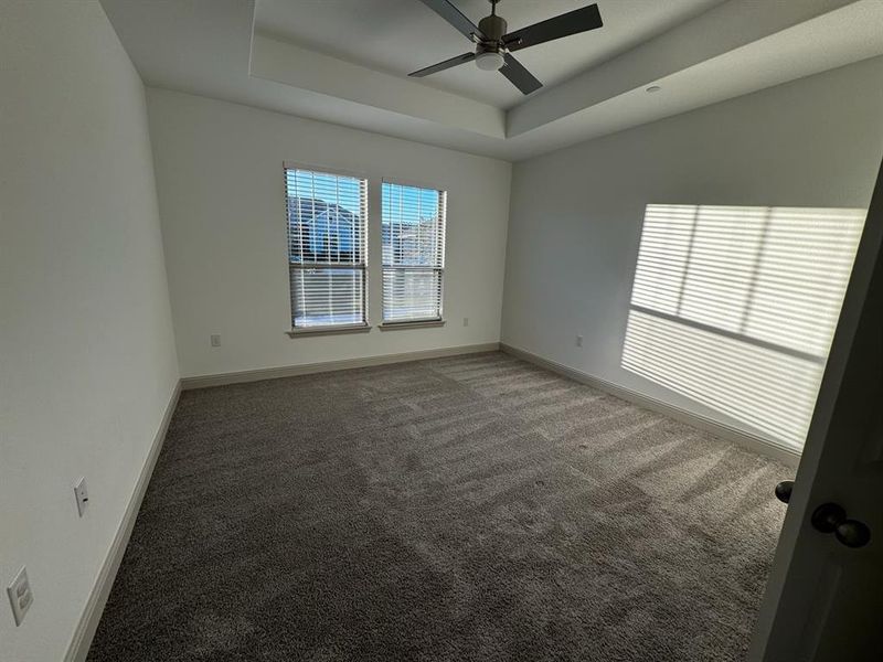 Spare room with dark colored carpet, ceiling fan, and a raised ceiling