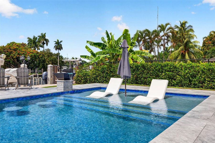 Salt chlorinated pool w/ water features, LED color changing light, sun shelf with umbrella hole and in water stools. Stone decking surrounds the pool