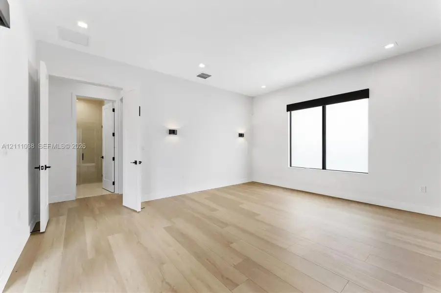 Neutral interior space featuring wood-finish flooring, recessed lighting, dual wall-mounted sconces, and a large window with a dark frame