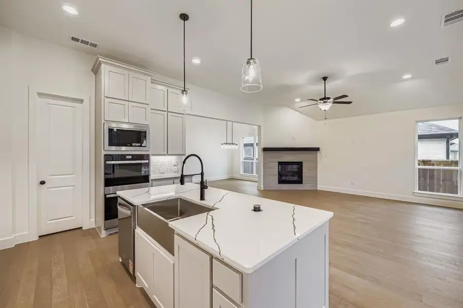 Kitchen with white cabinets, decorative light fixtures, open floor plan, light wood-style floors, and a center island with sink