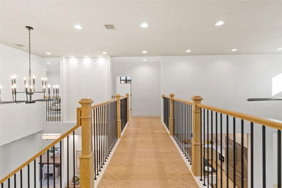 The upstairs landing makes a statement with warm wood floors, natural wood railings, and black iron balusters that overlook the living space below. Recessed lighting keeps the area bright, and the open layout adds a sense of flow—perfect for a reading nook, gallery wall, or just enjoying the architectural depth of the home.