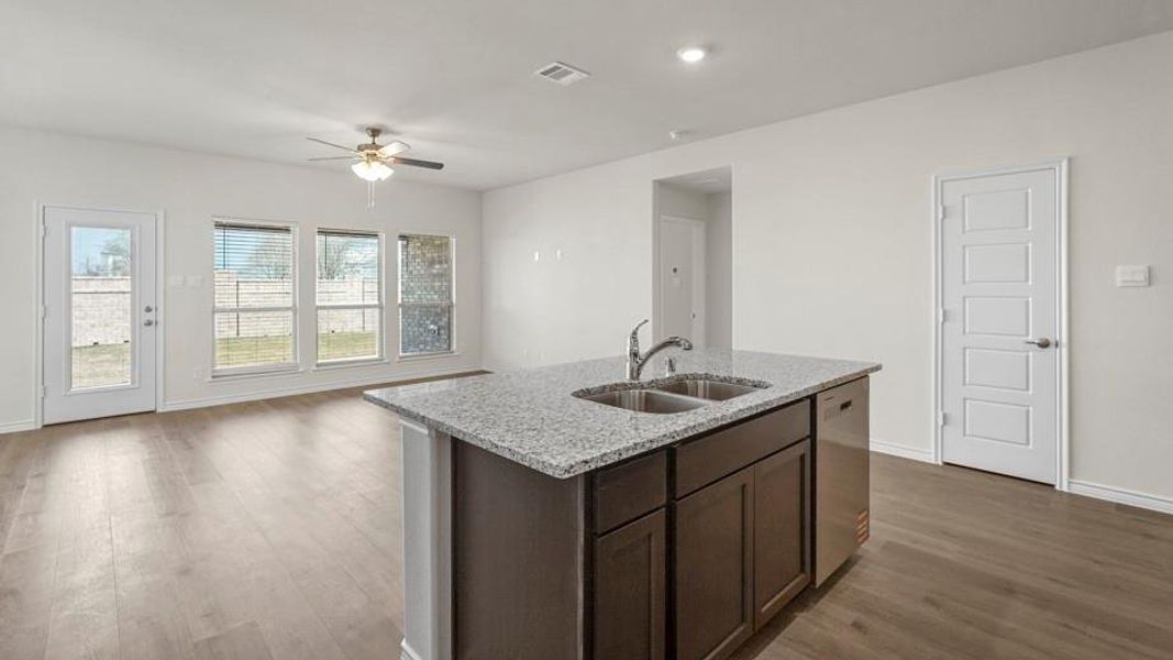 Open concept living space featuring light-colored flooring, a kitchen island with granite countertops and a double basin sink, and a ceiling fan